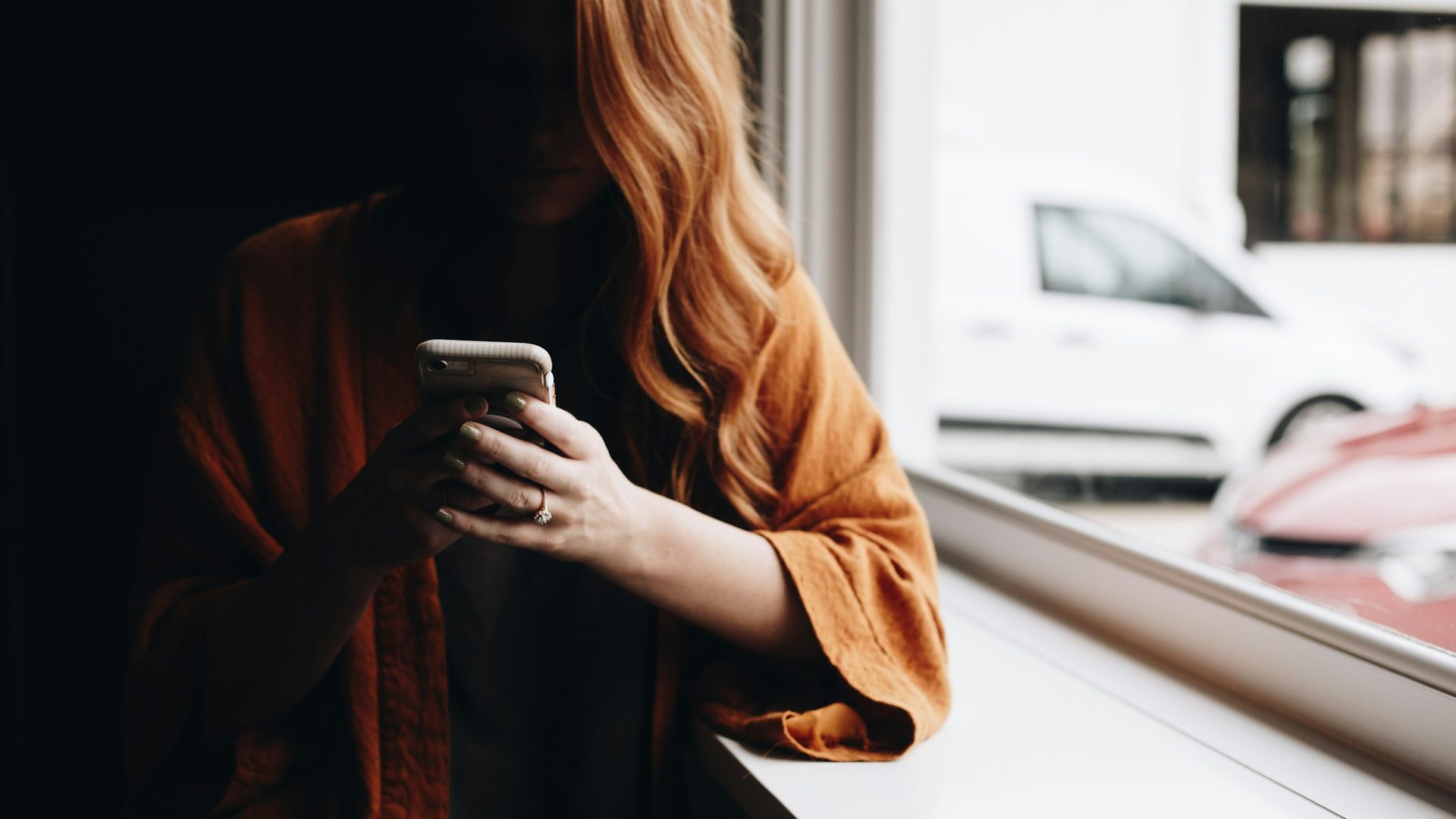 Donna accanto a una finestra che guarda lo smartphone, il volto in ombra